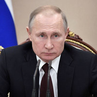 Vladamir Putin in suit and tie sitting on a panel and reading a question off what appears to be a heart shaped note