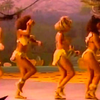 Everybody Walk the Dinosaur Four dancers dressed like cave women walking like dinosaurs