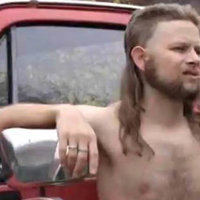 Almost Politically Correct Redneck zach downey shirtless with a mullet leaning on a red pickup truck