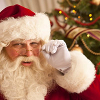 Santa Claus with a thick white beard and a red hat lowering his glasses