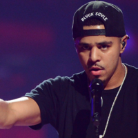 Rapper J. Cole with his hands outstretched in a "hold up" position