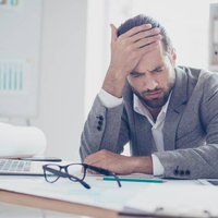 man at desk touching forehead with a pained expression