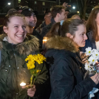 Taco Bell Vigil young adults in coats smiling and holding flowers