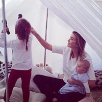 Ivanka Trump's #TogetherApart woman sitting in a blanket fort indoors holding a baby while a child plays with a flashlight