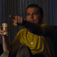 leonardo dicaprio as rick dalton in the film once upon a time in hollywood sitting on a couch in a yellow sweater and holding a beer and pointing his finger at the television screen.LoadOfBarnacles07
