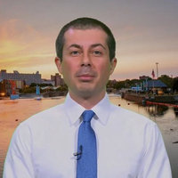 Mayor Pete Buttigieg in front of a skyline with a shaved head and wearing a white shirt and blue tie
