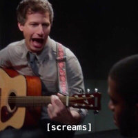 Andy Samberg as Jake Peralta playing guitar in the interrogation scene with subtitle screams