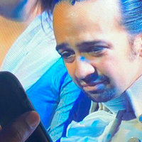 Lin-Manuel Miranda on TV Reading Off A Smartphone Lin Manuel Miranda on TV leaning forward as if to look at a phone held up by a person outside the TV