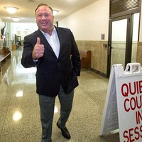 Alex Jones in a courthouse giving a thumbs up to the camera.