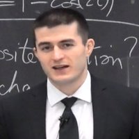 Lex Fridman in a suit in front a chalkboard.
