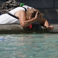 Woman using a fountain to refresh herself during a heat wave in the UK.