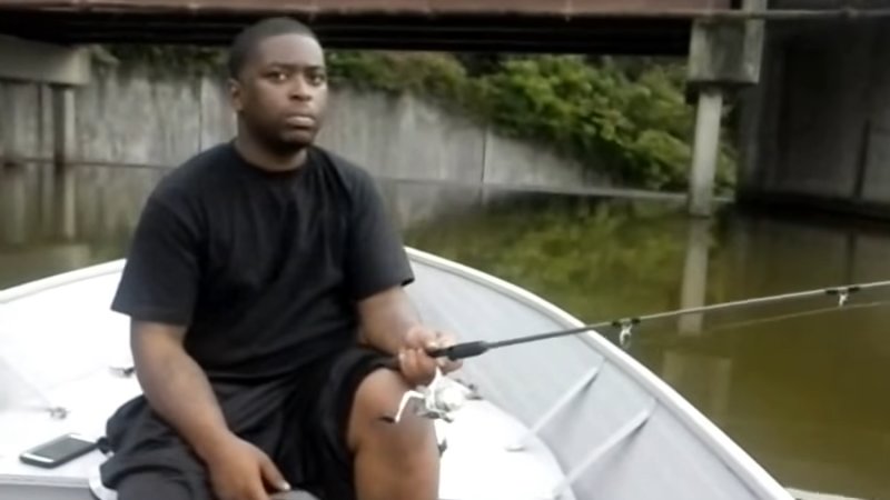 black guy holding a fishing rod in a boat looking at the viewer with concern