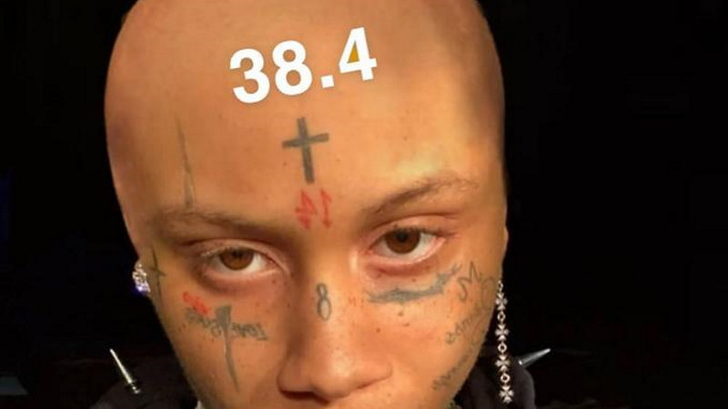 bald person with a cross tattooed on their forehead and several other facial tattoos and the number 38.4 written across their head