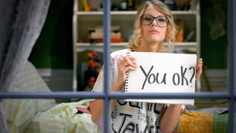 Taylor Swift in the you belong with me music video holding a sign that says "you ok?"