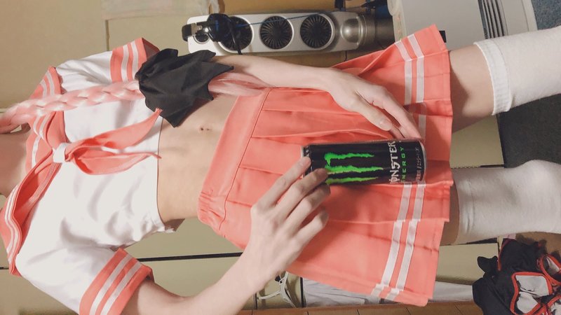 Person in a pink and white sailor costume holding a can of Monster energy drink over their crotch