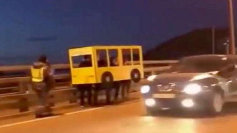 A Blursed Image of a group of people walking in a cardboard bus costume on the highway. 