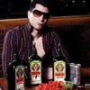 Guy in sunglasses and an open shirt sitting behind bottles of Jaegermeister bottles and Redbull cans