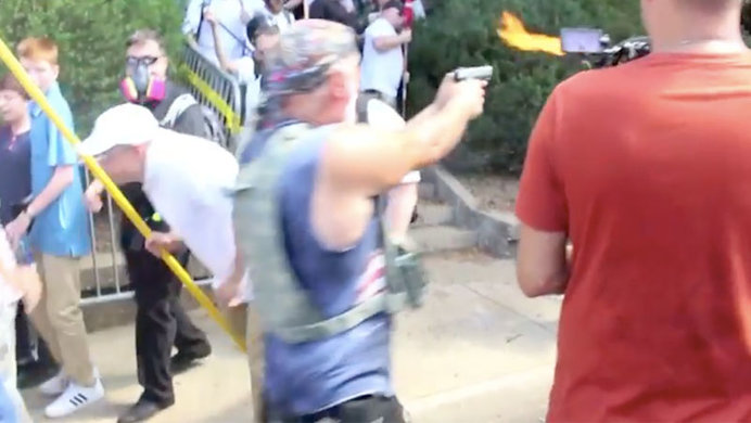 Screenshot of a man in a denim vest fires a silver pistol at counter-protesters at the Unite The Right rally in Charlottesville, Virgina.  