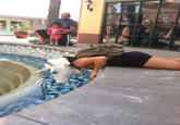 woman wearing a unicorn mask lying by a public outdoor fountain as if drinking from the crisp blue water