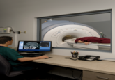 Original 2009 stock image uploaded to Shutterstock by James Steidel, titled, "Technician Monitoring MRI Scan." The image later led to the "How Does It Look, Doc?" "exploitable":https://knowyourmeme.com/memes/exploitables meme, which shows a person wearing red scrubs lying down in an MRI machine, asking, "How does it look, doc?" or "Does it look bad, doc?" to which the doctor to responds, "Lmao, hold on fam," or "hold on dude," while distracted by a video game, meme or piece of media on his computer screen. 