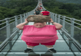 An HD "GIF":https://knowyourmeme.com/memes/cultures/gif of a woman in a pink shirt jumping backward with a big rock on a glass bridge to break the bridge from a viral "AI Video":https://knowyourmeme.com/memes/cultures/ai-video. 
