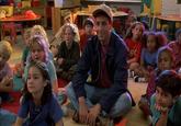 An image from the movie Billy Madison. It shows Adam Sandler as Billy Madison sitting amongst his classmates in the first grade, listening to the teacher read a story.