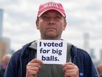 An AI-generated image of a man in a MAGA hat holding a paper with the words "I voted for big balls" on it, referencing DOGE staffer Edward "Big Balls" Coristine