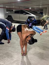 A photoshop of Rubi Rose bending over in a parking garage in front of her Cybertruck. Some nodders have been added to the scene.