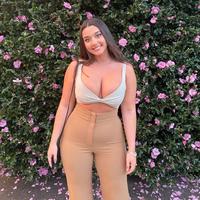 A photo allegedly of Zoe Kalotheos. She is posing in front of some flowers.
