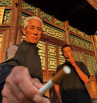 A photo of a Chinese man offering you a c--------. Another Chinese man smokes in the background.