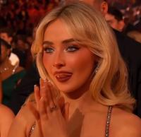 Sabrina Carpenter with her tongue out licking her lips. She is watching Bad Bunny accept his Album of the Year award at the Grammys 2026.