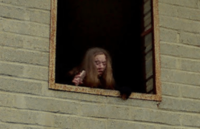 Very odd looking woman looking out an abandoned building