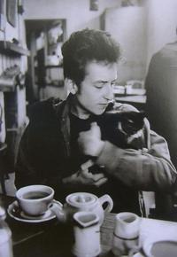 Bob Dylan holding a small cat while sitting at a table with coffee cups and a teapot in Greenwich Vi...