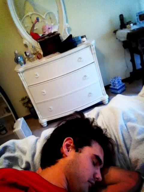 Man faking that he is napping as we can see his hand holding up the phone in the dresser mirror behind him