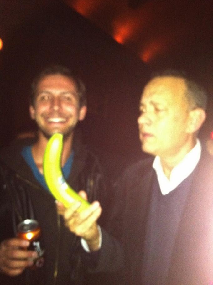 man smiling next to tom hanks looking perplexed at a banana for scale