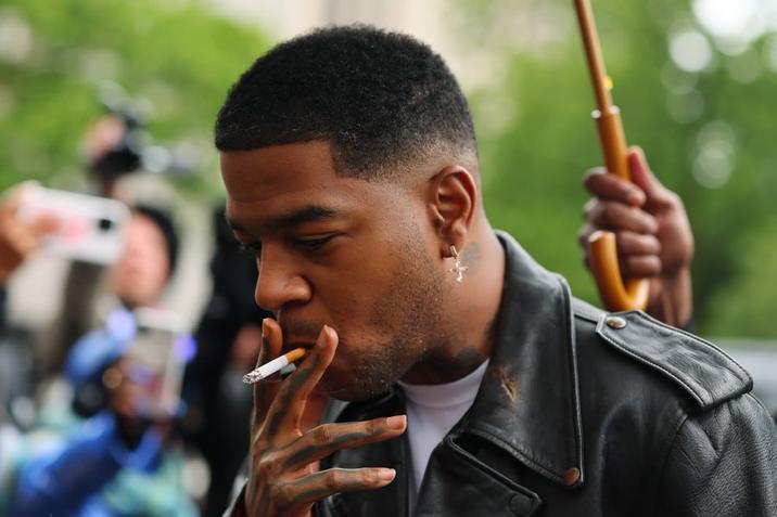 A series of images taken by Michael M. Santiago showing Kid Cudi arriving at Manhattan Federal Court to testify against Diddy began making the rounds on May 22nd, showing him dressed in a black leather jacket, blue jeans, and smoking a c--------. 