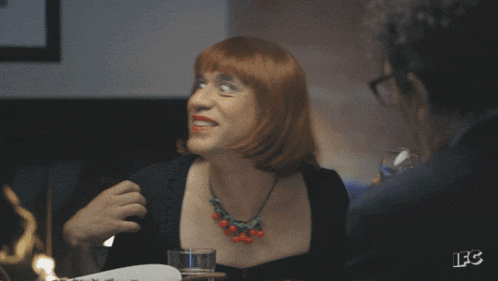 The GIF of Fred Armisen in a red wig looking around and smiling comes from the March 17th, 2016, episode of _Portlandia_, "Lance is Smart." The episode featured a sketch where Lance and Nina are at a dinner party, where Nina keeps sharing irrelevant and droll personal anecdotes. The GIF of Nina looking around the table appears at roughly the 6:44 timestamp. 