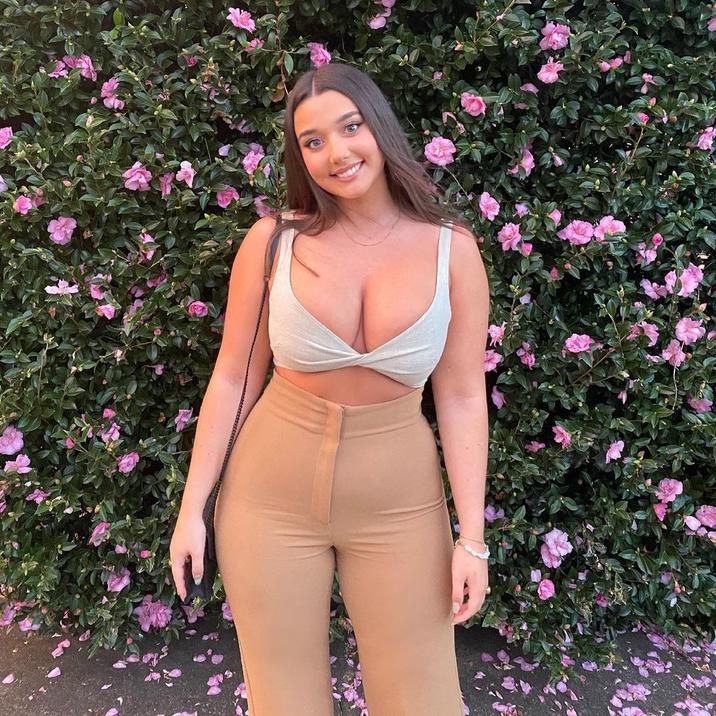 A photo allegedly of Zoe Kalotheos. She is posing in front of some flowers.