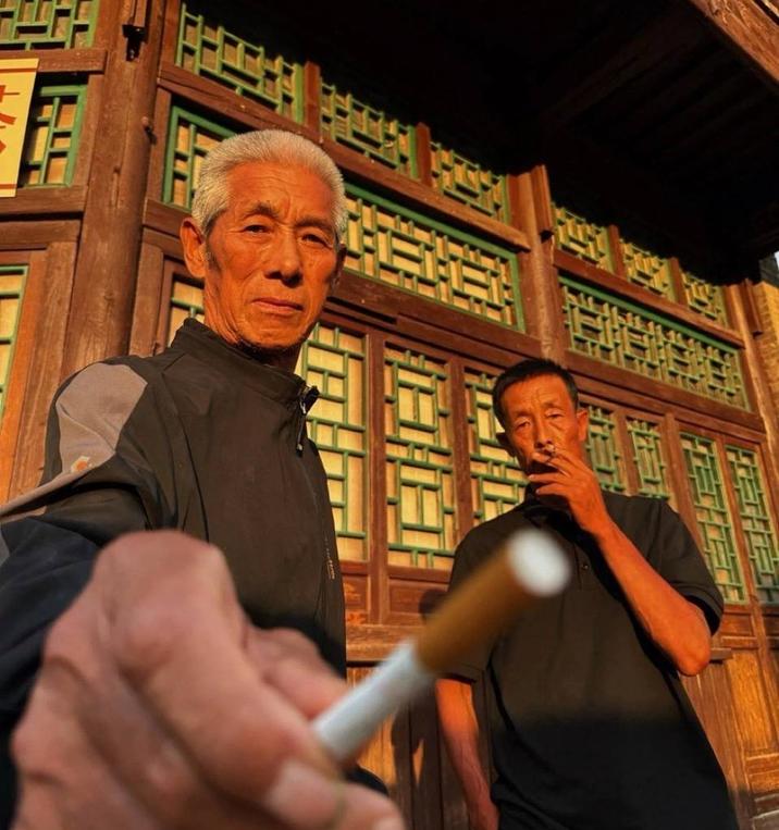 A photo of a Chinese man offering you a c--------. Another Chinese man smokes in the background.