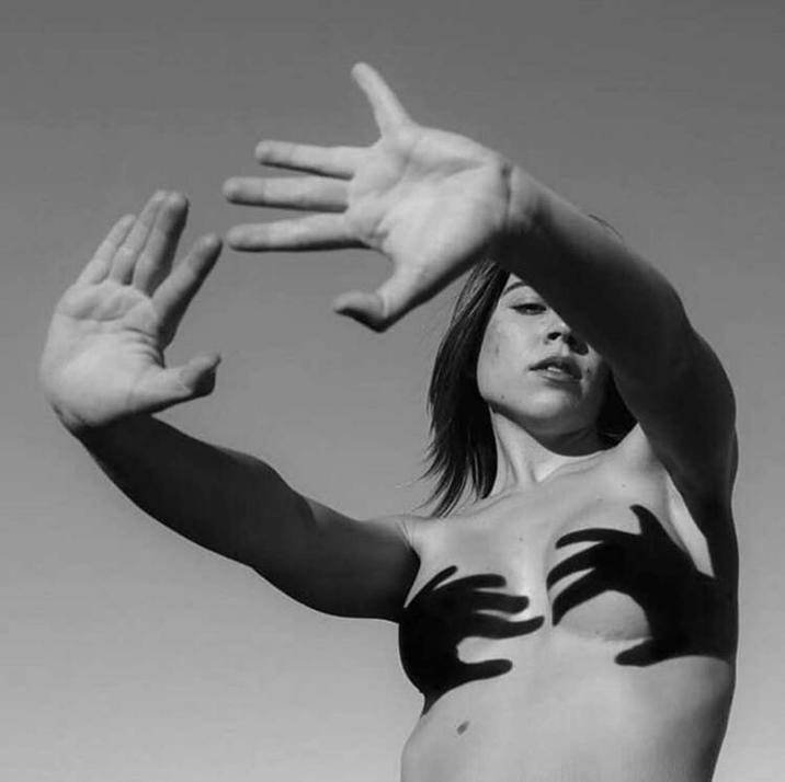 A photograph of a woman using the shadows of her hands to cover her breasts.
