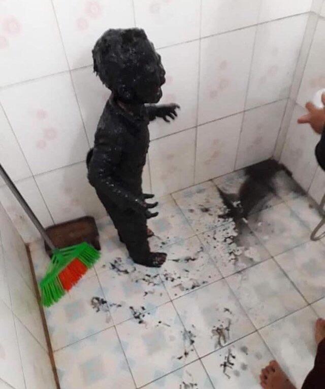 A photo of a kid covered head-to-toe in black mud. The context is that the kid fell in a puddle of mud when he got up to pee in the garden one night in Vietnam.