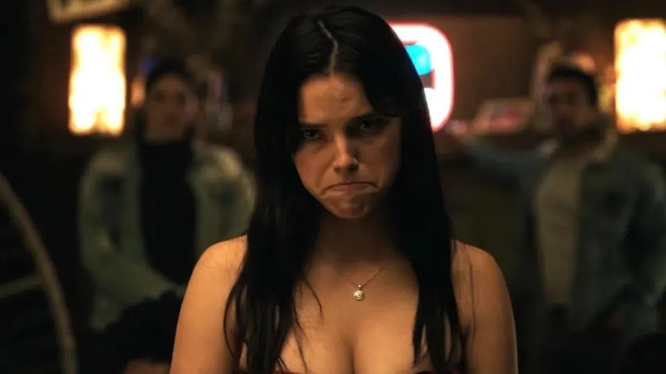 An image of Nikki from the 2026 horror movie "Obsession" frowning or pouting. She is sitting at a dinner table in a restaurant.