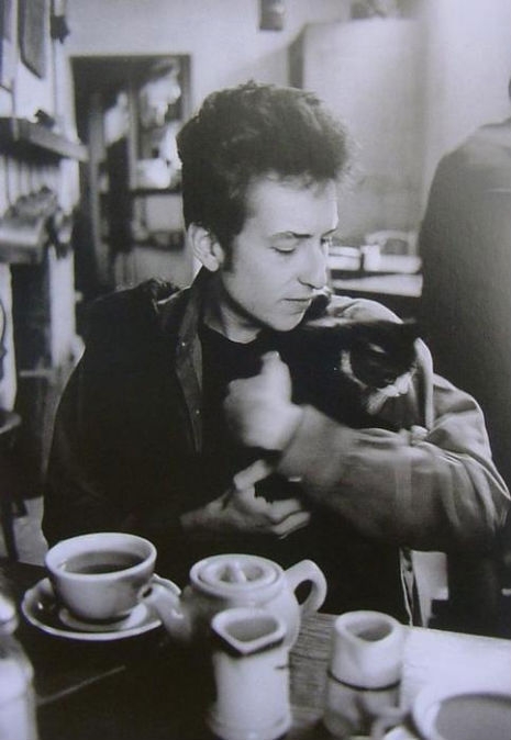 Bob Dylan holding a small cat while sitting at a table with coffee cups and a teapot in Greenwich Vi...